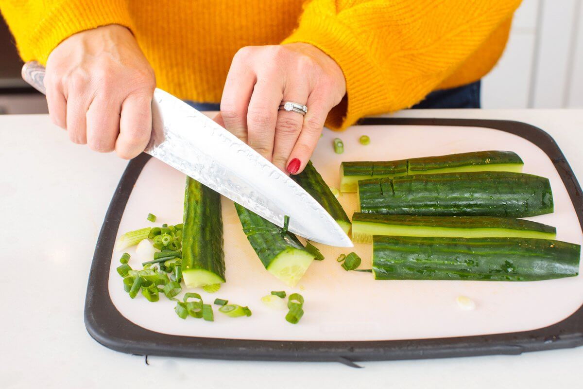 Liz using a knife to smash quartered cucumber.