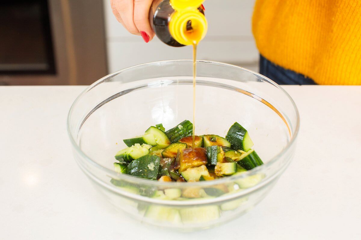 Pouring sesame oil into a bowl with smashed cucumbers.