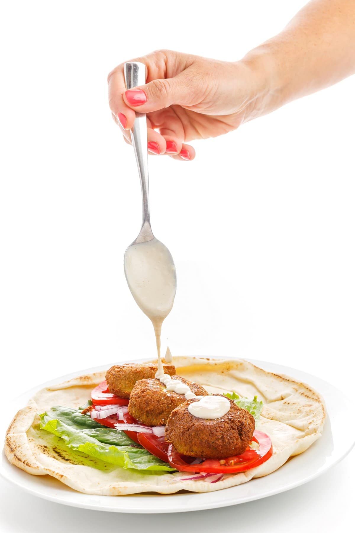 Drizzling tahini sauce with a spoon onto authentic Lebanese falafel in an open pita wrap.