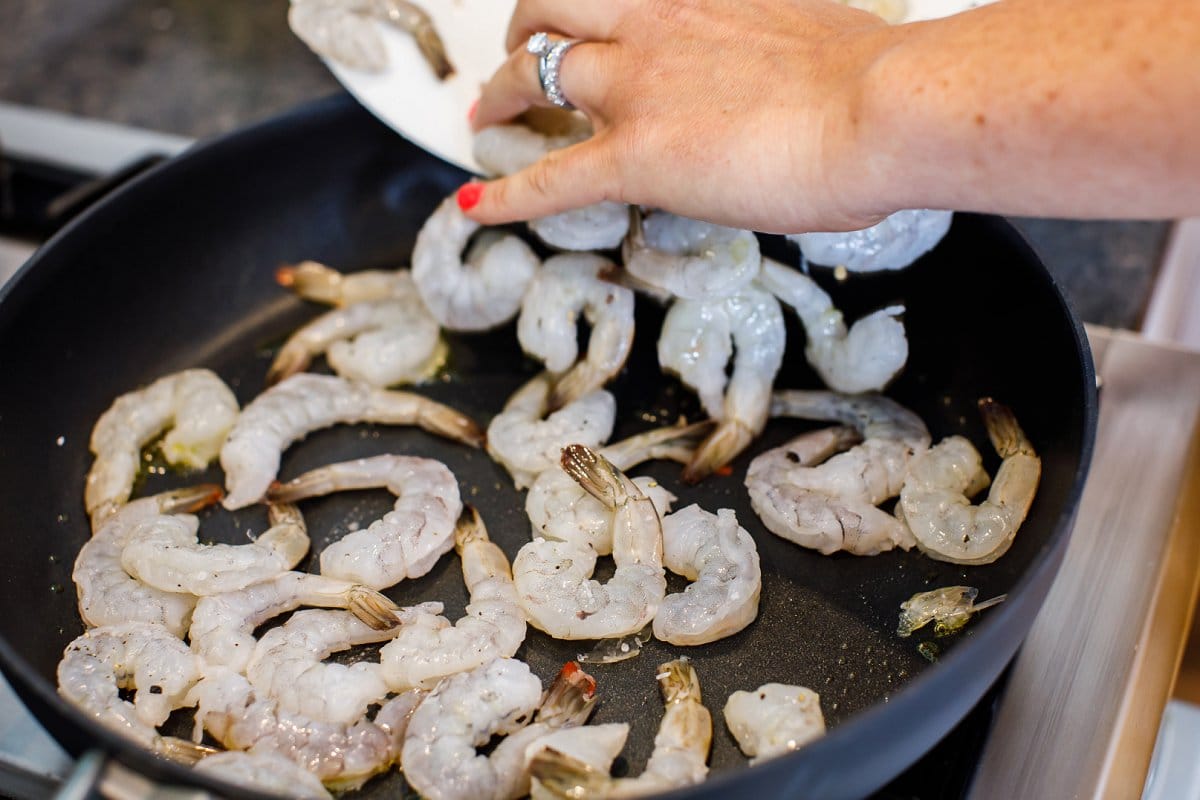Adding raw shrimp to a hot skillet on the stove.