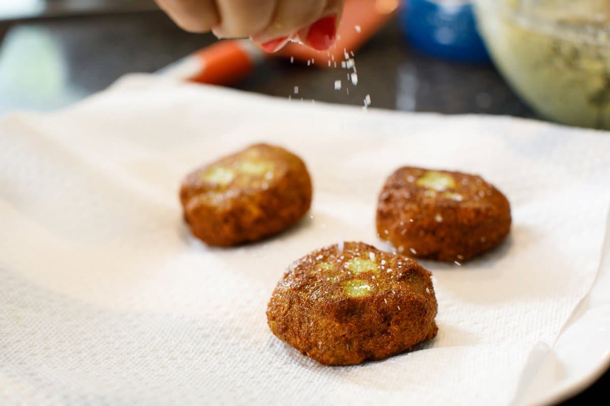 Sprinkling fried falafel patties with kosher salt.