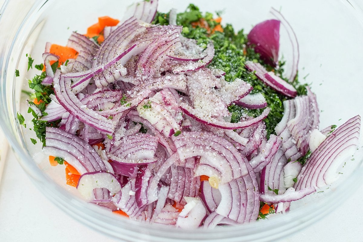 Bowl of cut carrots, sliced onions, and fresh herbs.