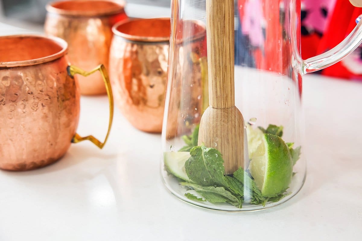 Muddling lime and mint in the bottom of a pitcher.