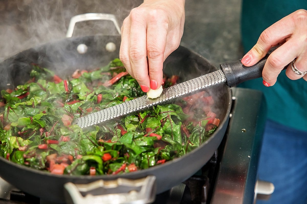 Liz freshly grating garlic into the pan of sautéed swiss chard.