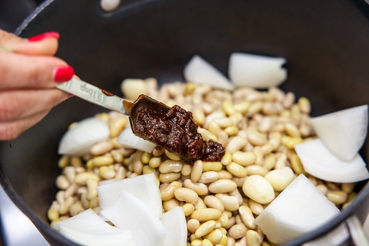 Adding onion and chipotle peppers to beans in pot.