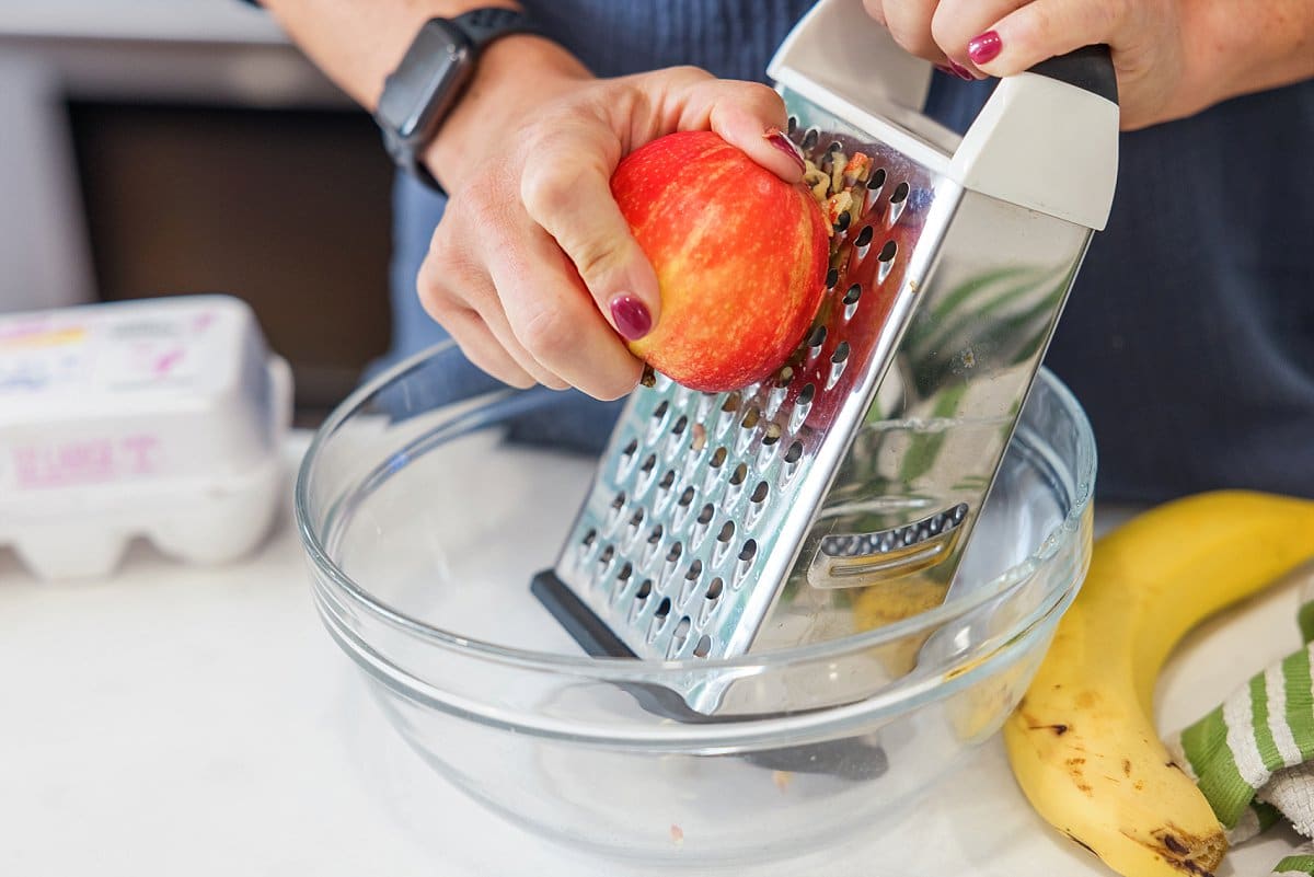 Liz grating an apple with a cheese grater into a glass bowl.