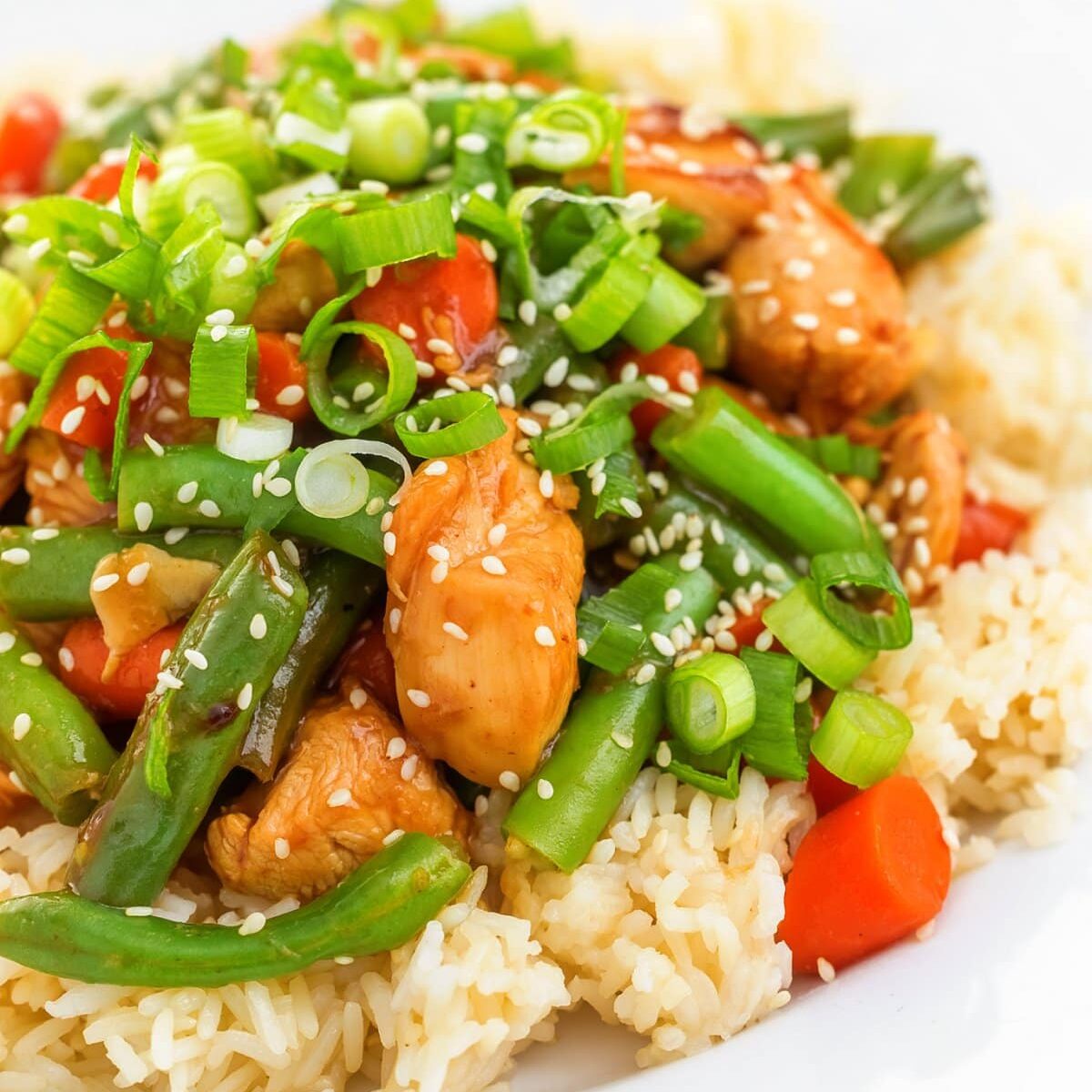 A plate of food with chicken and green beans and sesame seeds