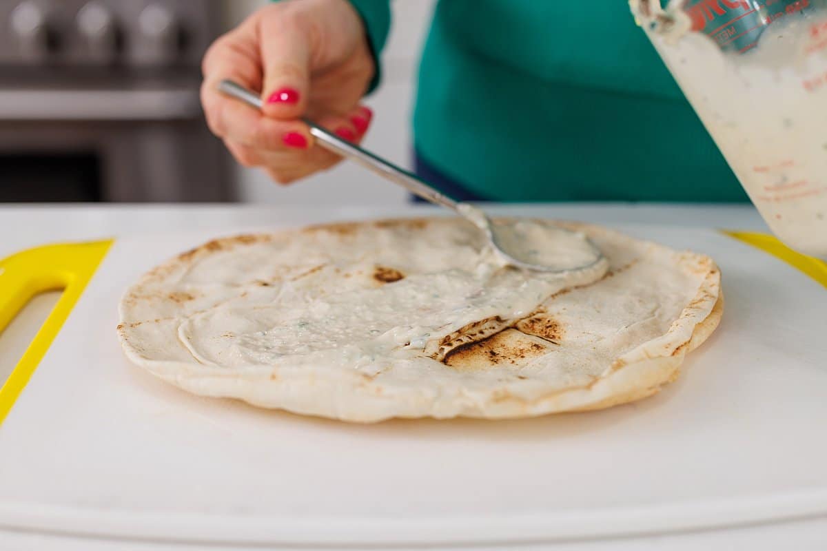 Spreading tahini sauce onto pita with a spoon.