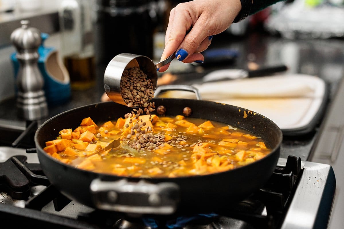 Adding lentils to skillet with sweet potatoes.