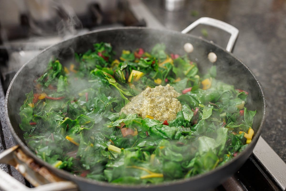 Dollop of pesto added to cooked swiss chard in pan.