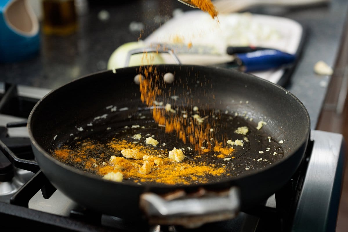 Adding seasoning to oil and garlic in pan.