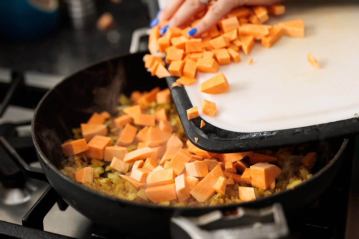 Adding cut up sweet potatoes to skillet with onion.