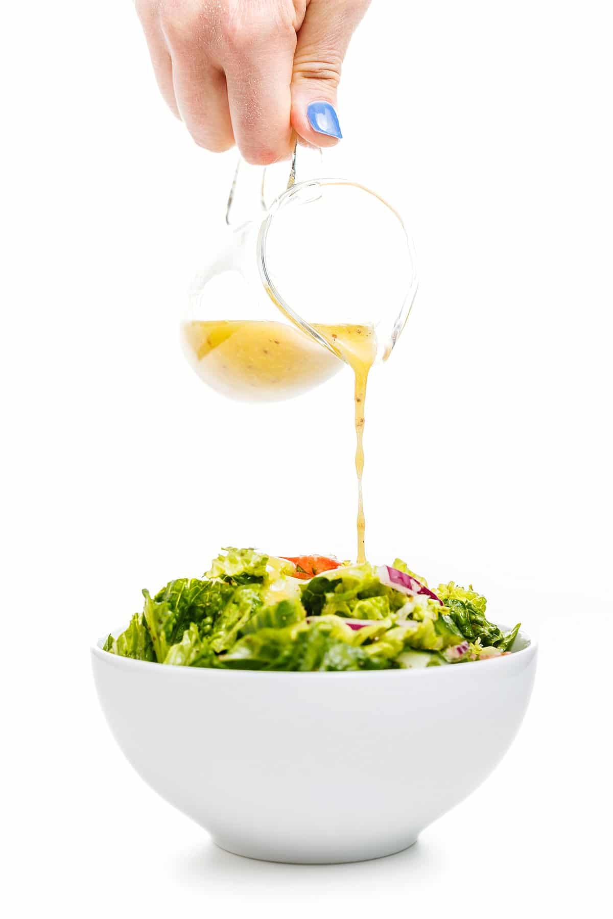Pouring lemon garlic Dijon vinaigrette over the top of a green salad in a white bowl.