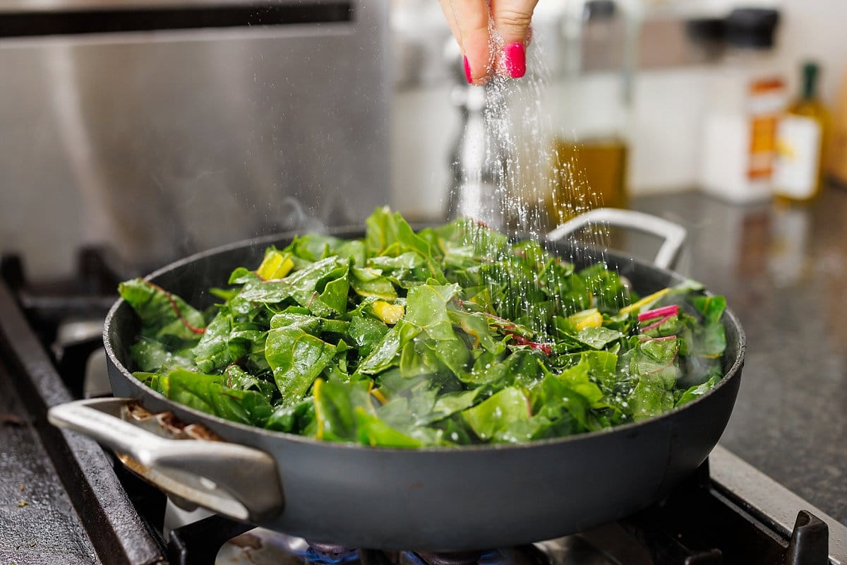 Seasoning chopped swiss chard in a pan.