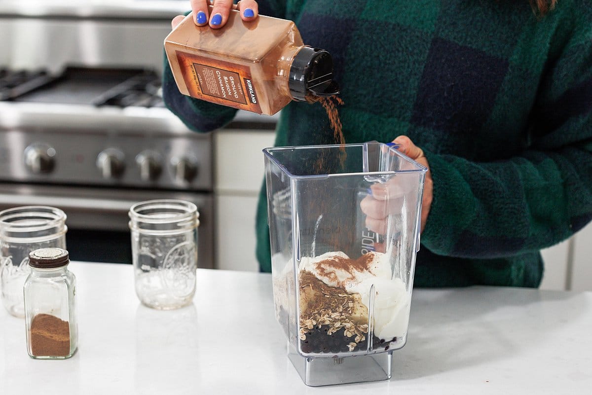 Sprinkling cinnamon into blender with smoothie ingredients.