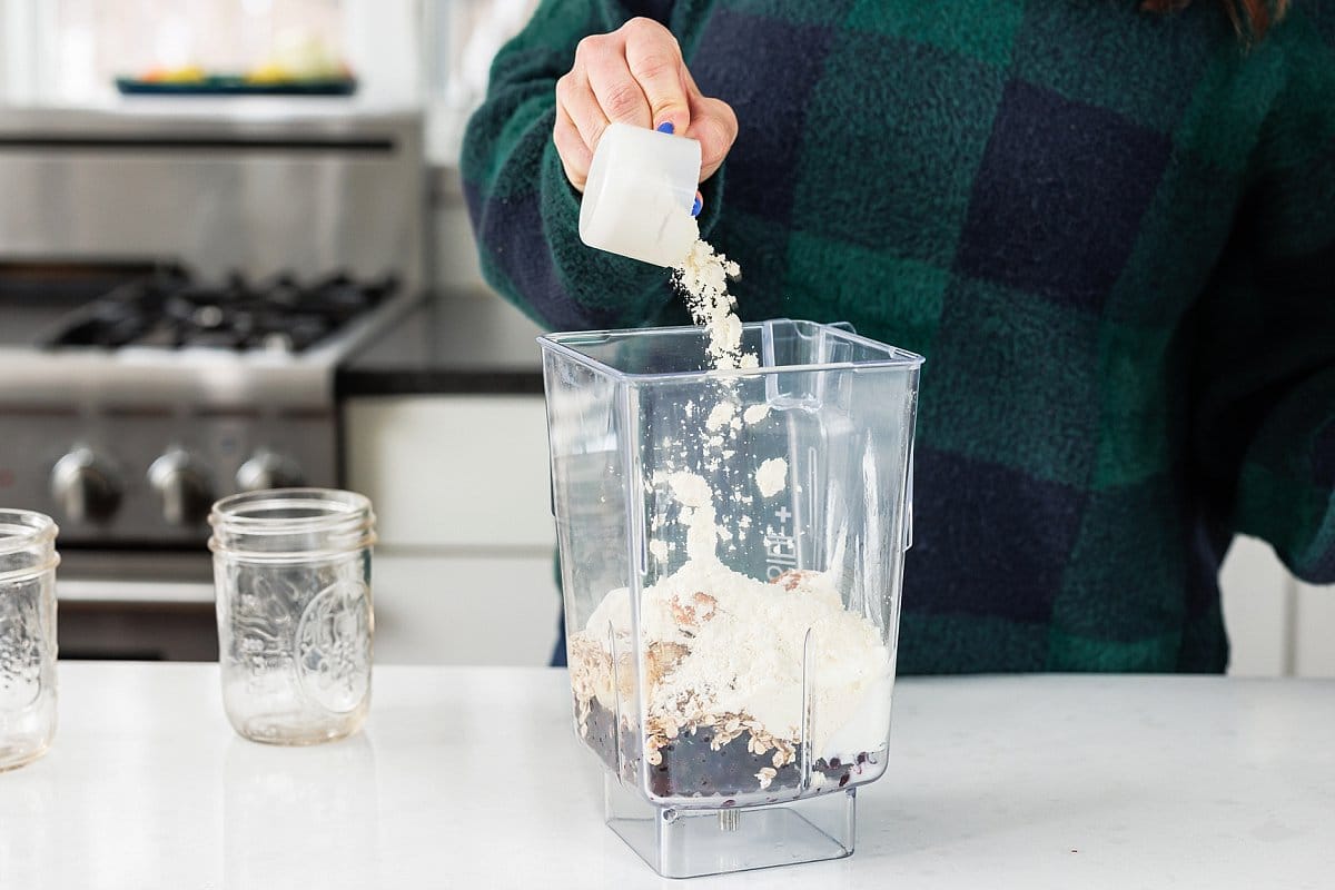 Adding a scoop of protein powder to bender with fruit and yogurt.