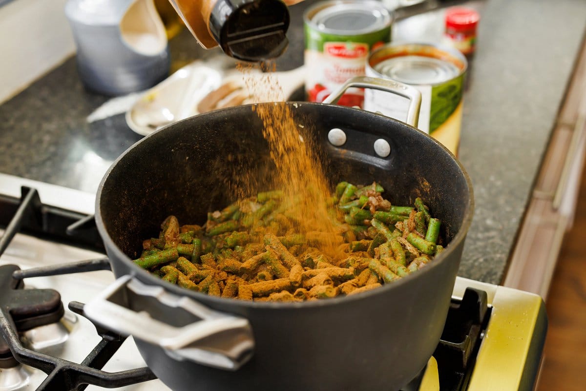 Adding Lebanese spice blend to green beans in a pot.