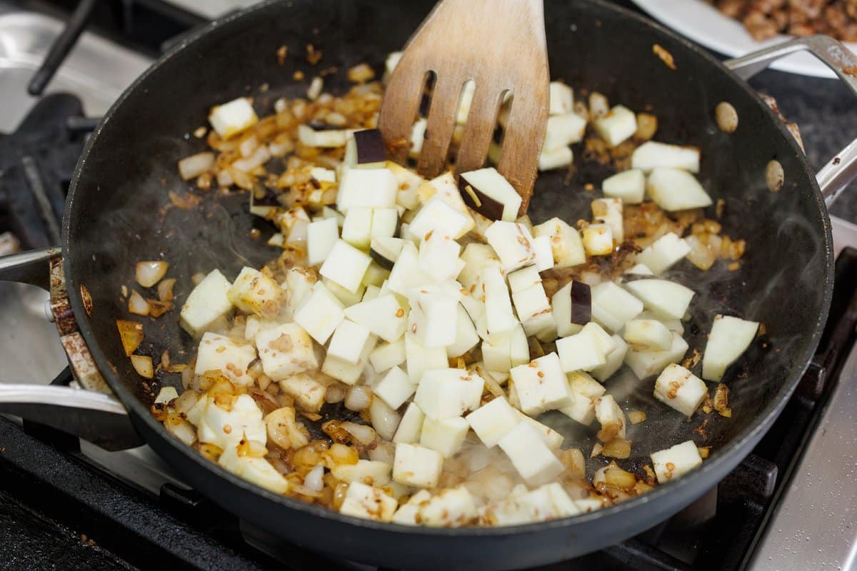 Adding cubed eggplant to skillet with cooked, diced onion.