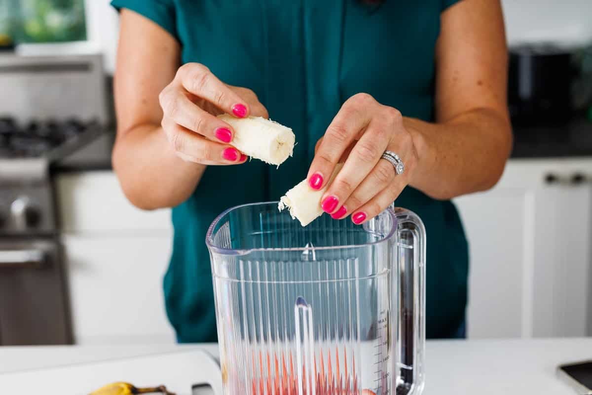 Adding banana halves to blender with strawberries.