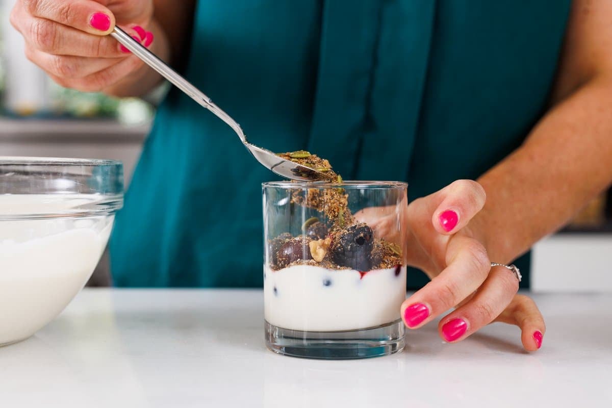 Adding granola mix on top of berries and yogurt.