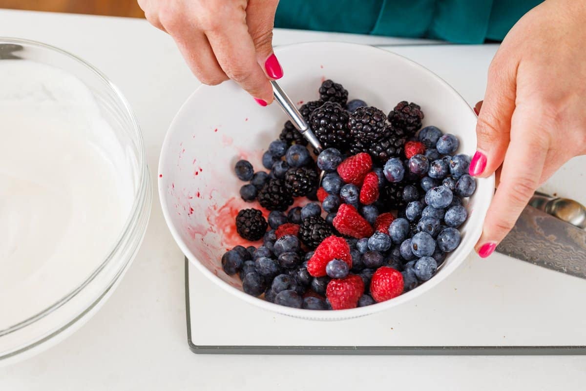 Gently stirring mixed berries in a white bowl.