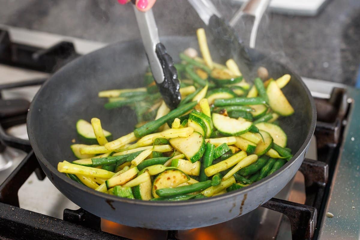 Tossing zucchini and green beans cooking in pan.