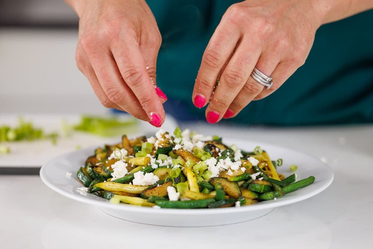 Crumbling feta cheese over the top of sautéed vegetables.