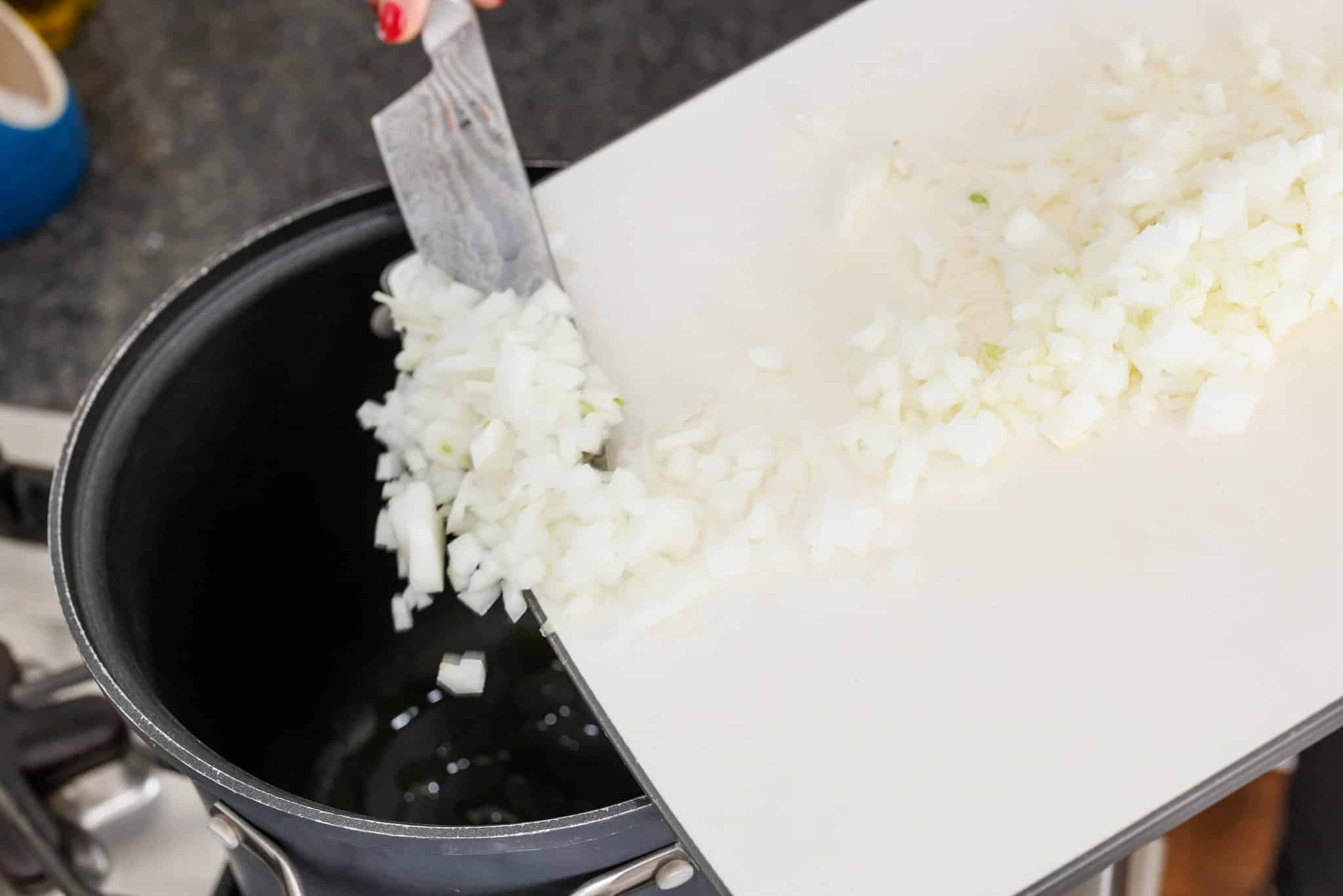 Adding diced onion to pot from cutting board.