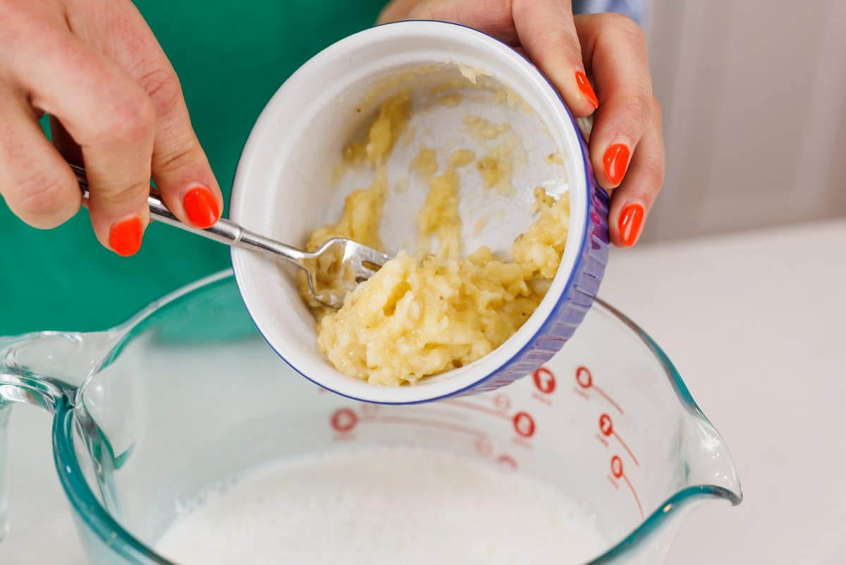Spilling mashed banana out of a small glass dish into a large measuring bowl.