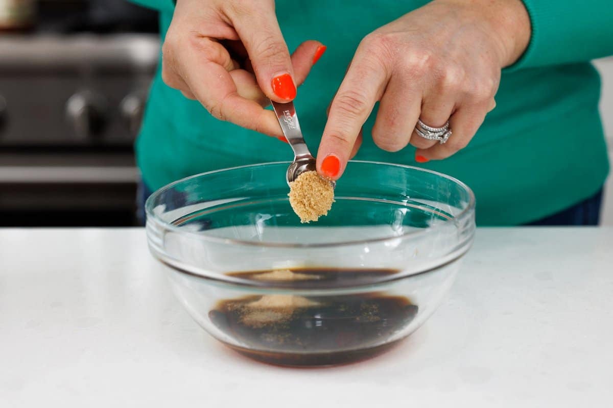 Adding brown sugar to dressing in bowl.