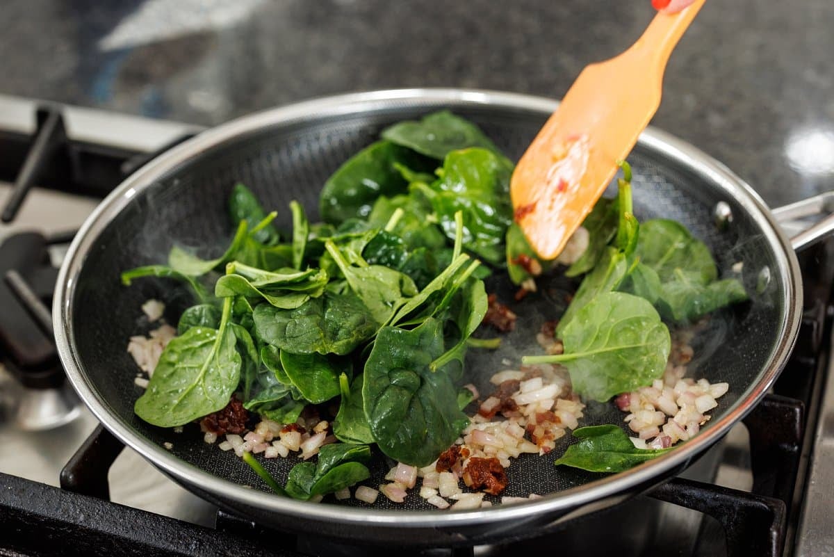 Baby spinach added to  a pan.