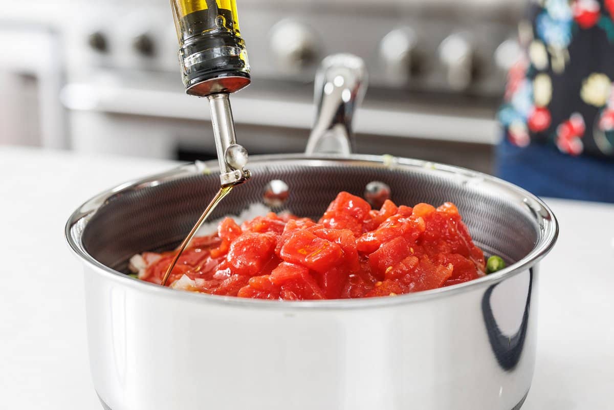 Drizzling olive oil over the top of diced tomatoes in pot.