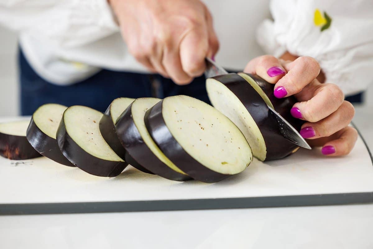 Liz slicing eggplant into discs on a cutting board.