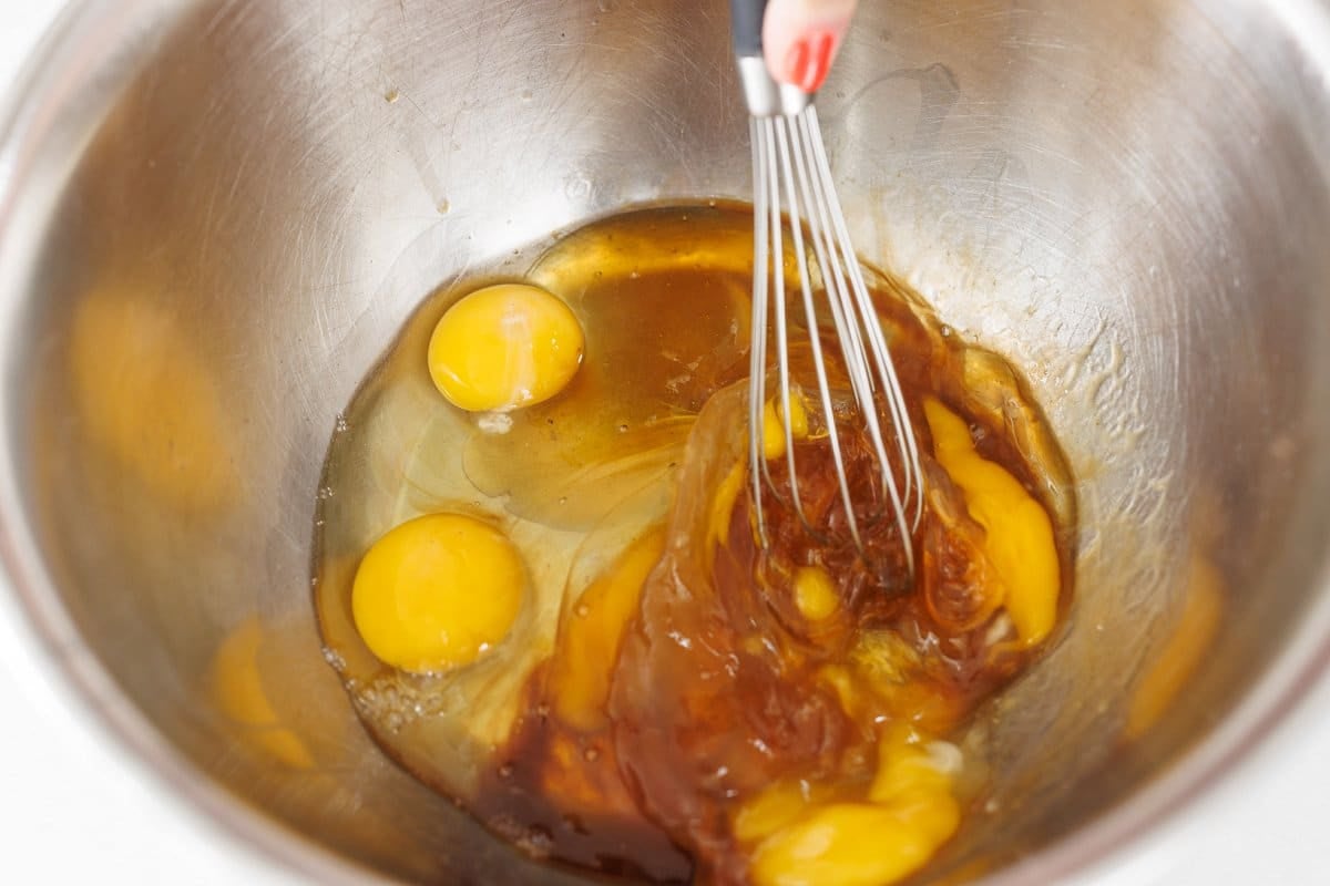 Whisking eggs with honey and vanilla in a large metal bowl.