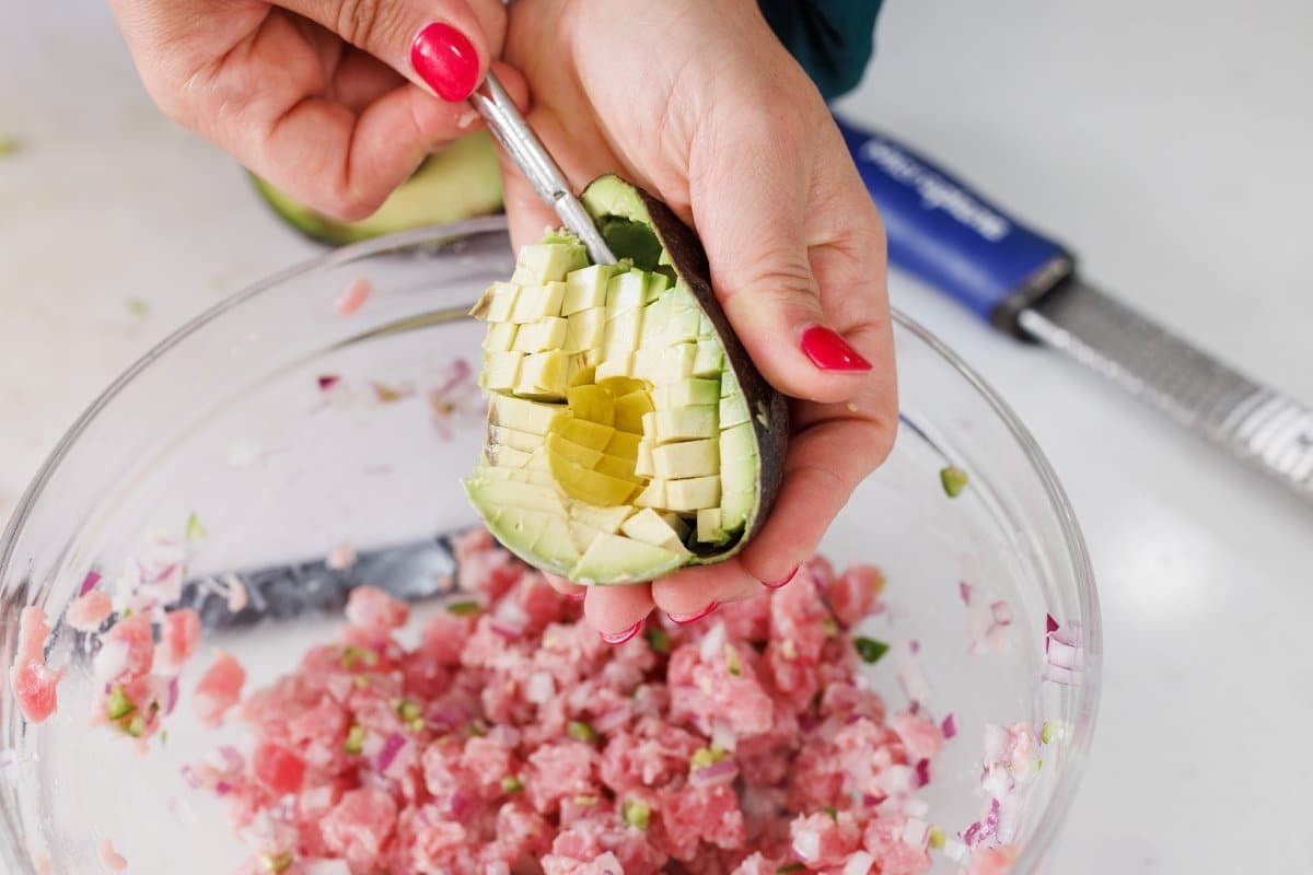 Scooping diced avocado to bowl with tuna.