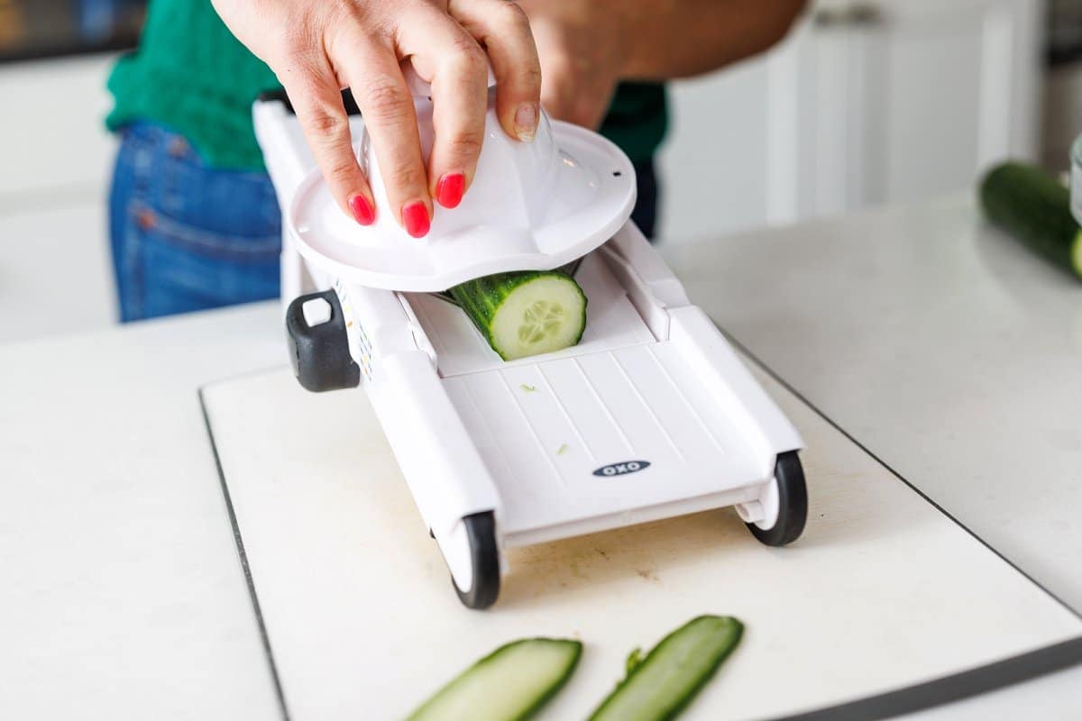 Using a mandolin to slice cucumbers into long strips.