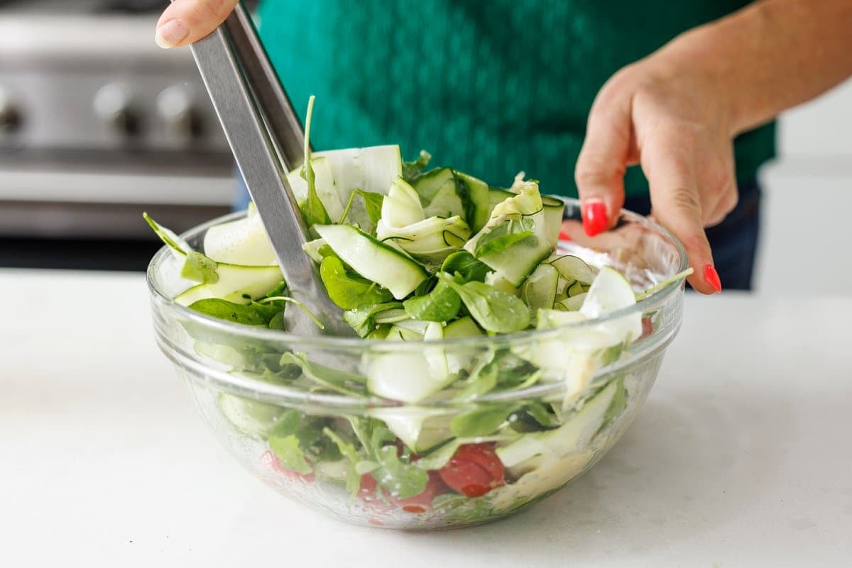 Using tongs to toss salad in dressing.