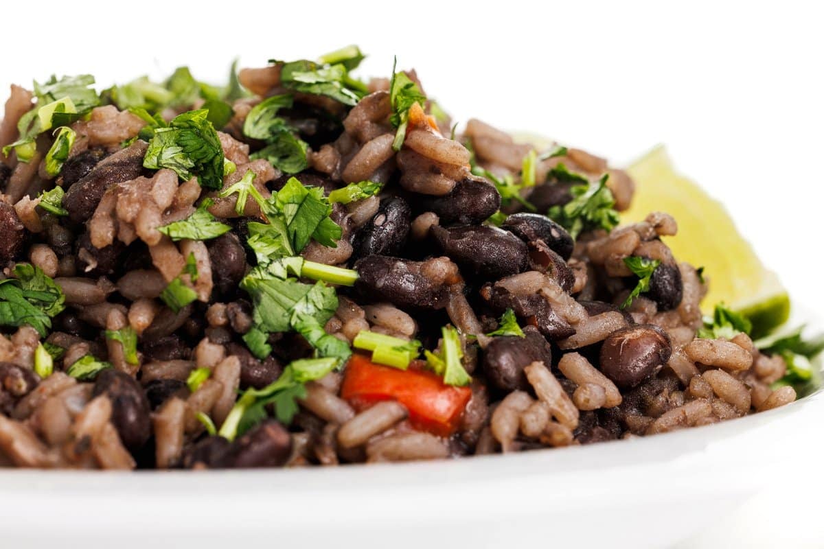 Close up, side view of Cuban black beans and rice with cilantro and lime wedges.