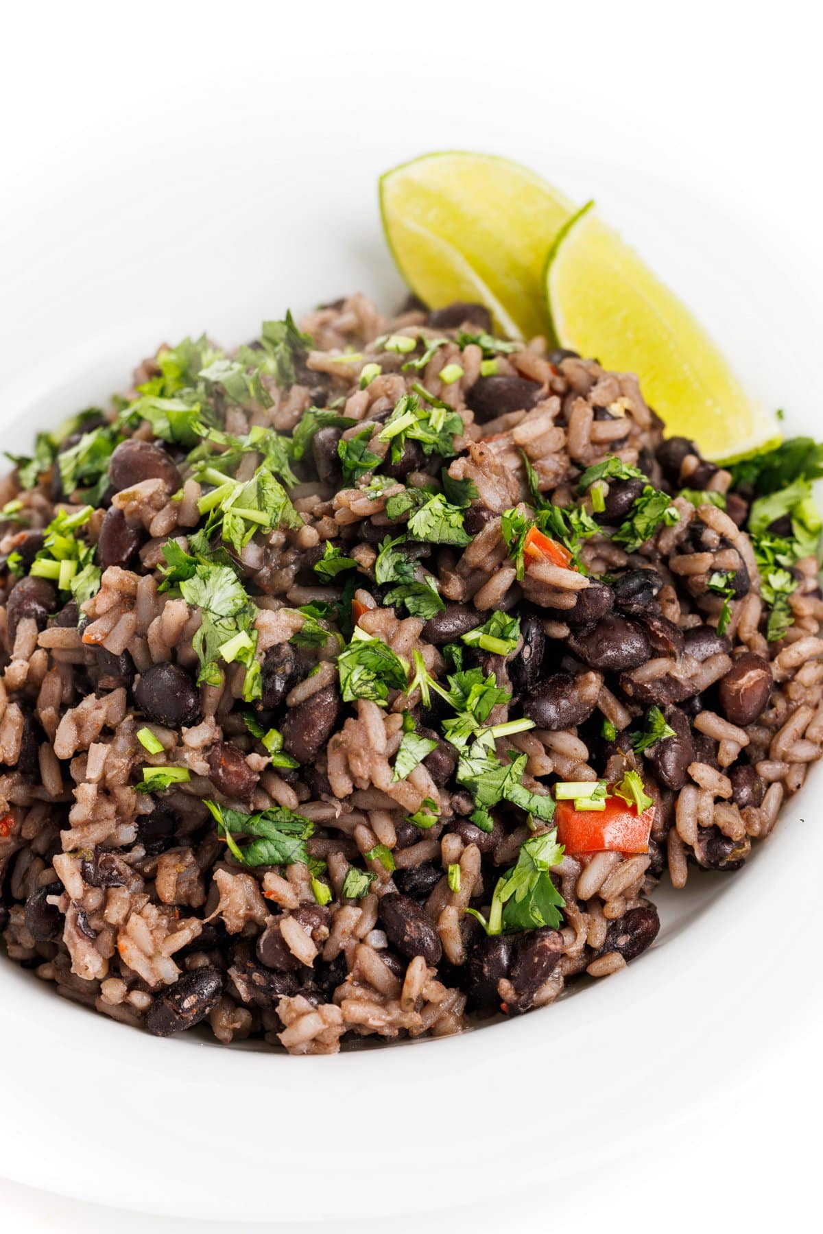 Cuban black beans and rice in a bowl garnished with fresh cilantro and lime wedges.