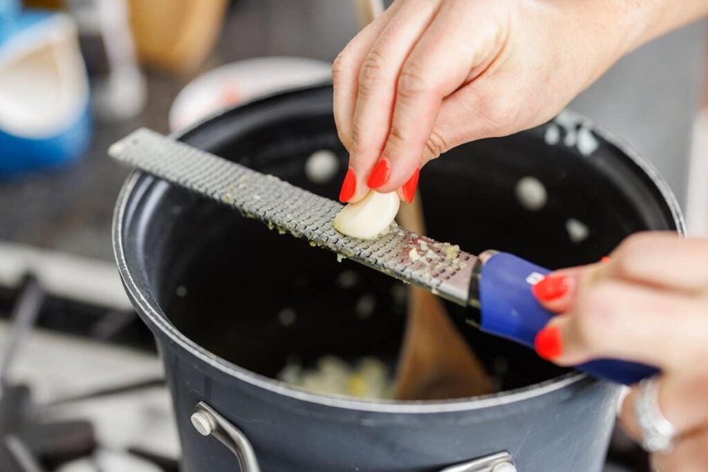 Using a microplane to grate garlic into a large pot.