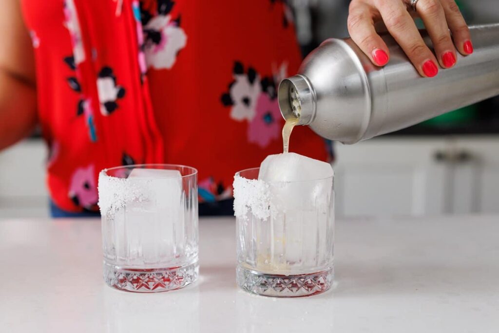 Liz pouring shaken margaritas into glasses from a cocktail shaker.