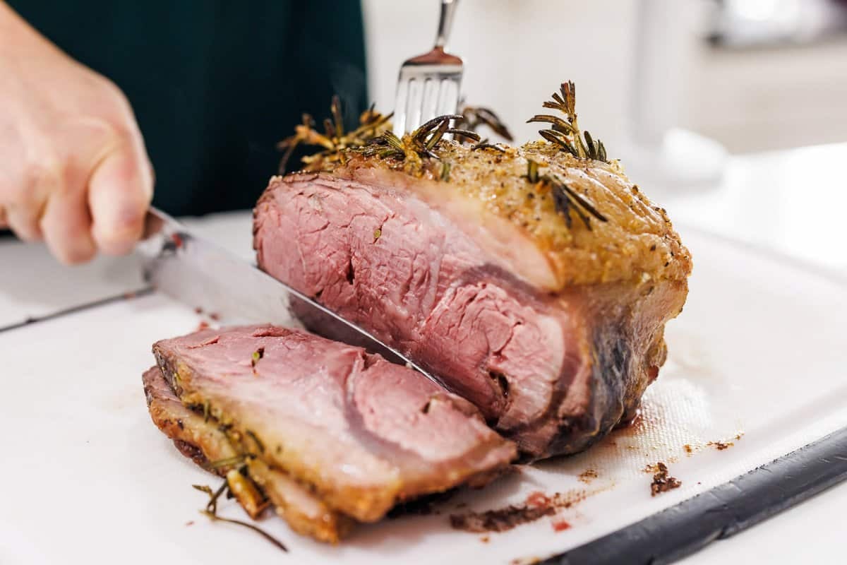 Cutting cooked Garlic and Rosemary Studded Beef Roast on a large cutting board.