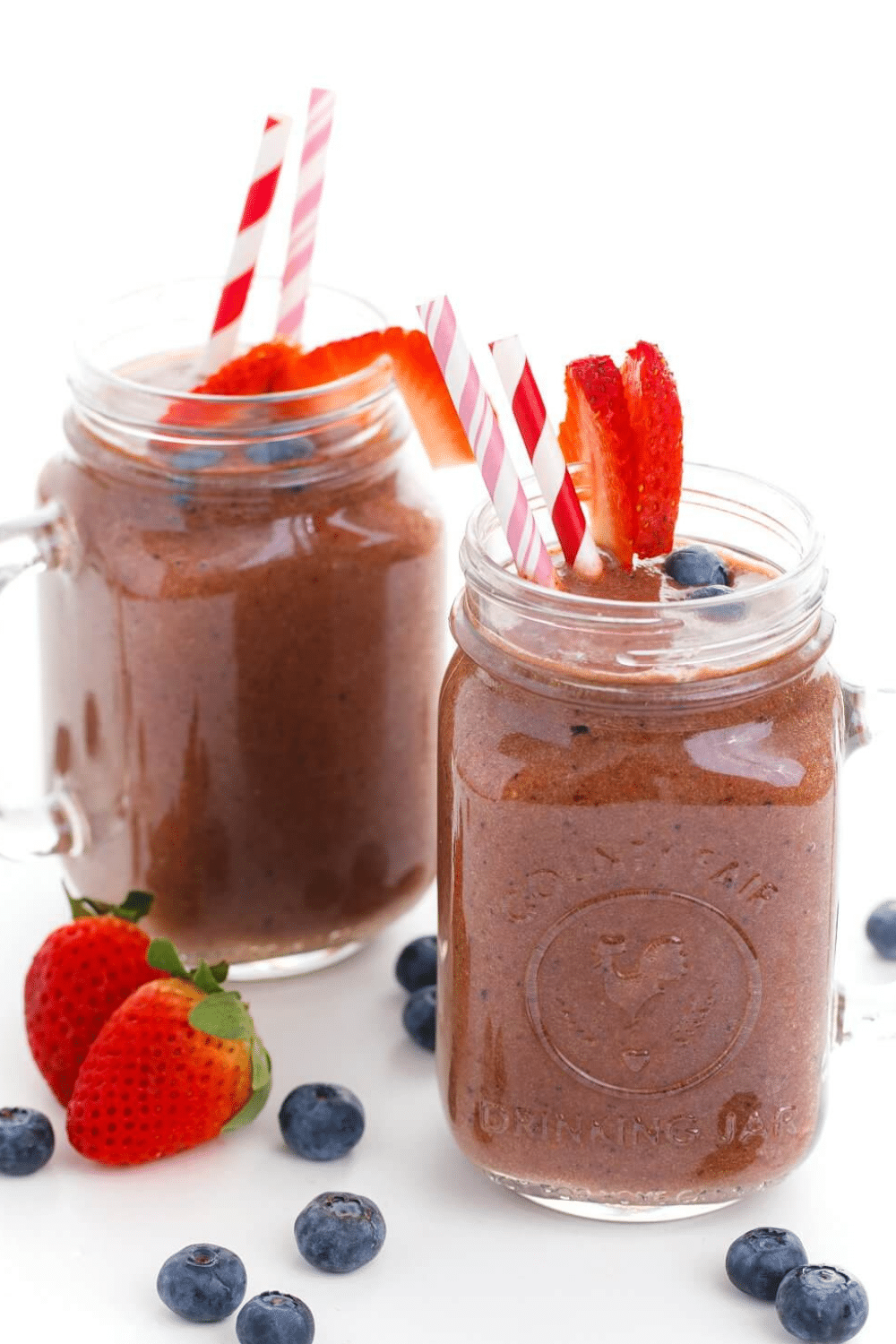 Two glasses of ginger berry smoothie with straws and strawberries.