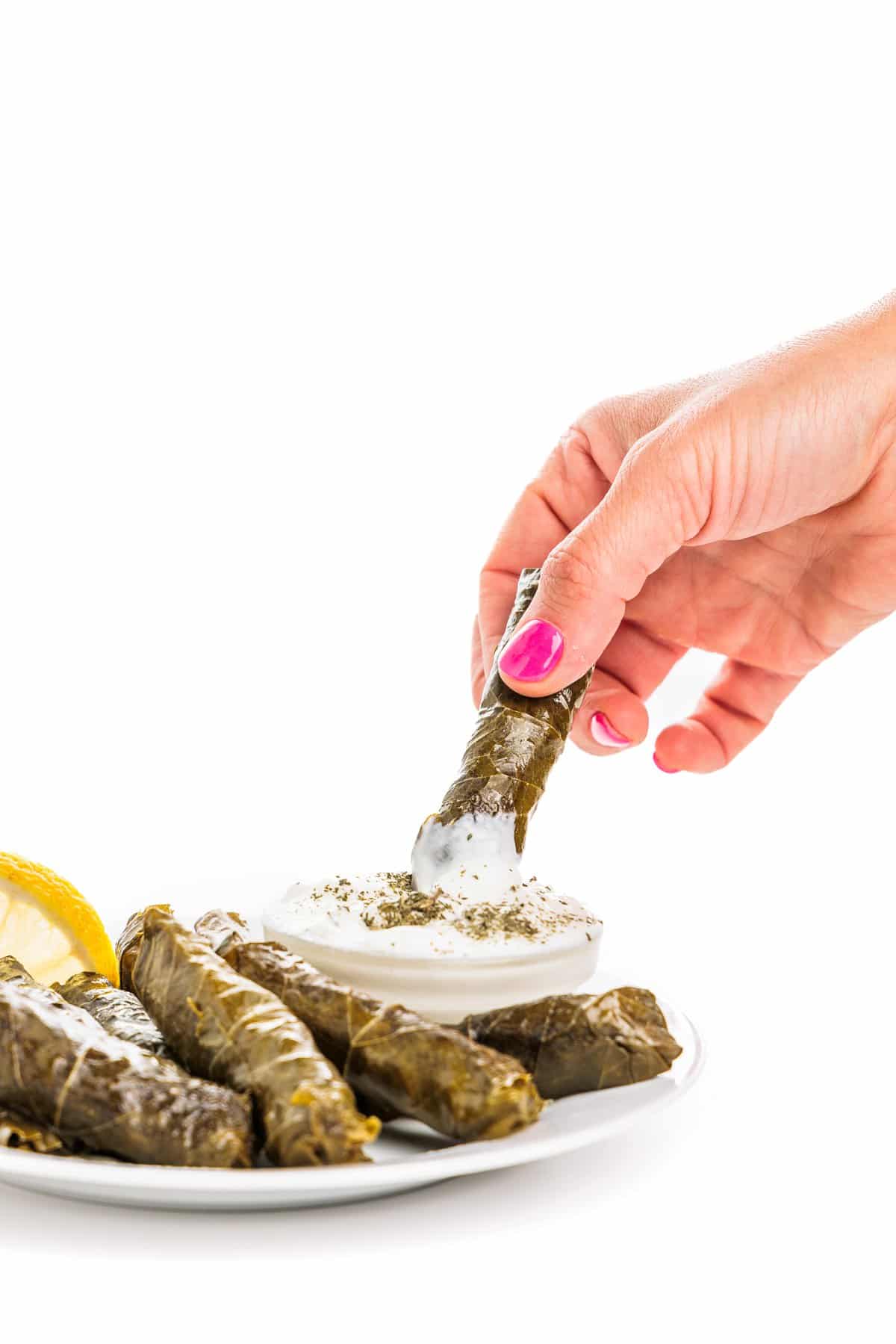 Hand dipping Lebanese meat stuffed grape leaves in cucumber laban.