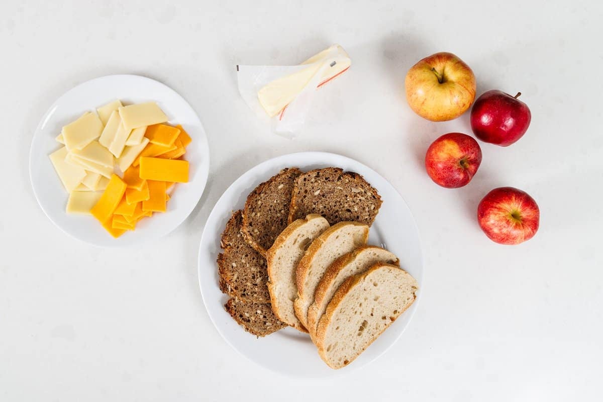 Ingredients for grilled cheese sandwich with apples against white background.