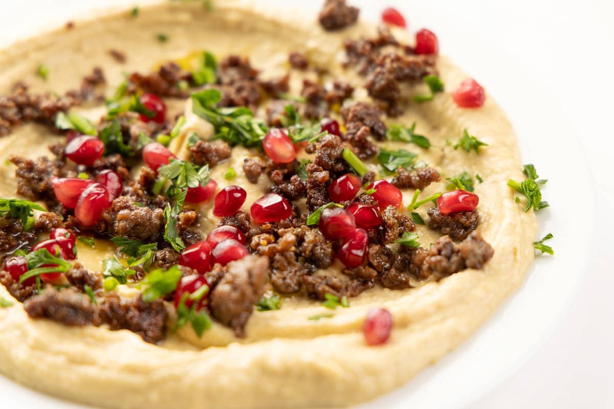 Topping hummus with cooked ground lamb, pomegranate seeds, and parsley.