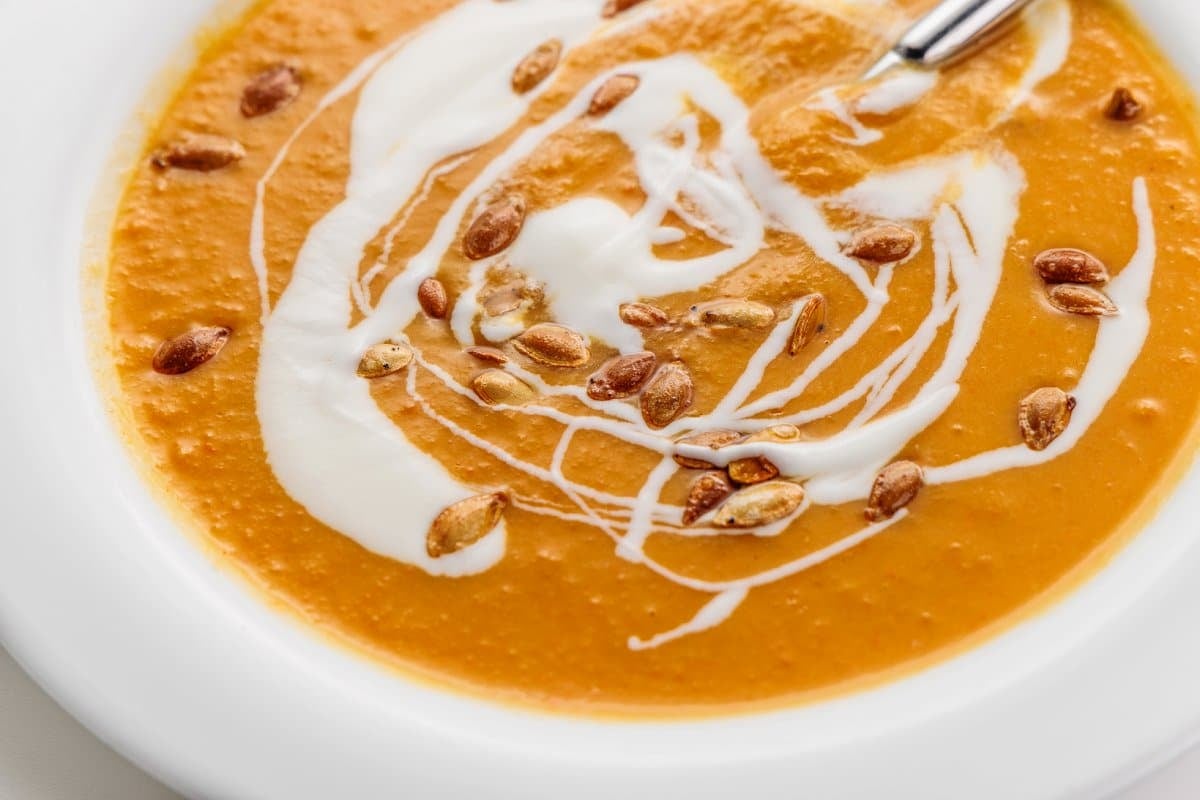 A spoon sitting in a bowl of roasted root vegetable soup in a white bowl.