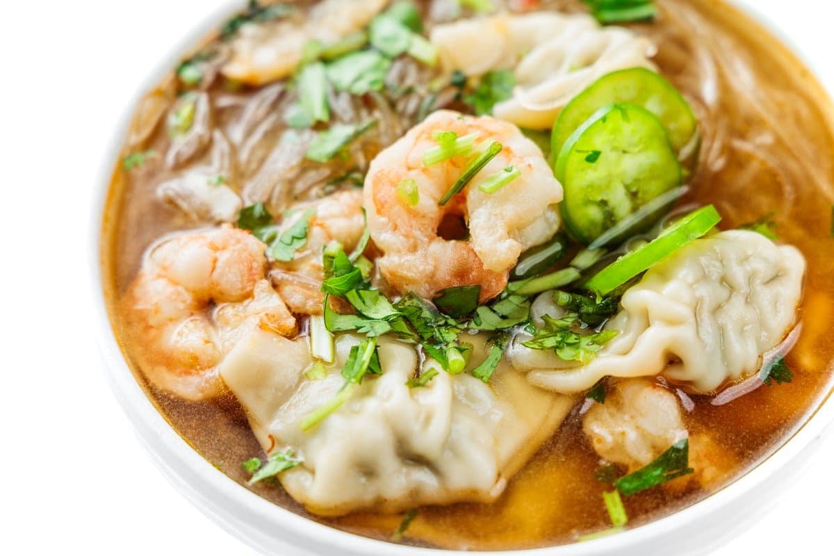 Asian noodle soup with shrimp and wontons in a white bowl.