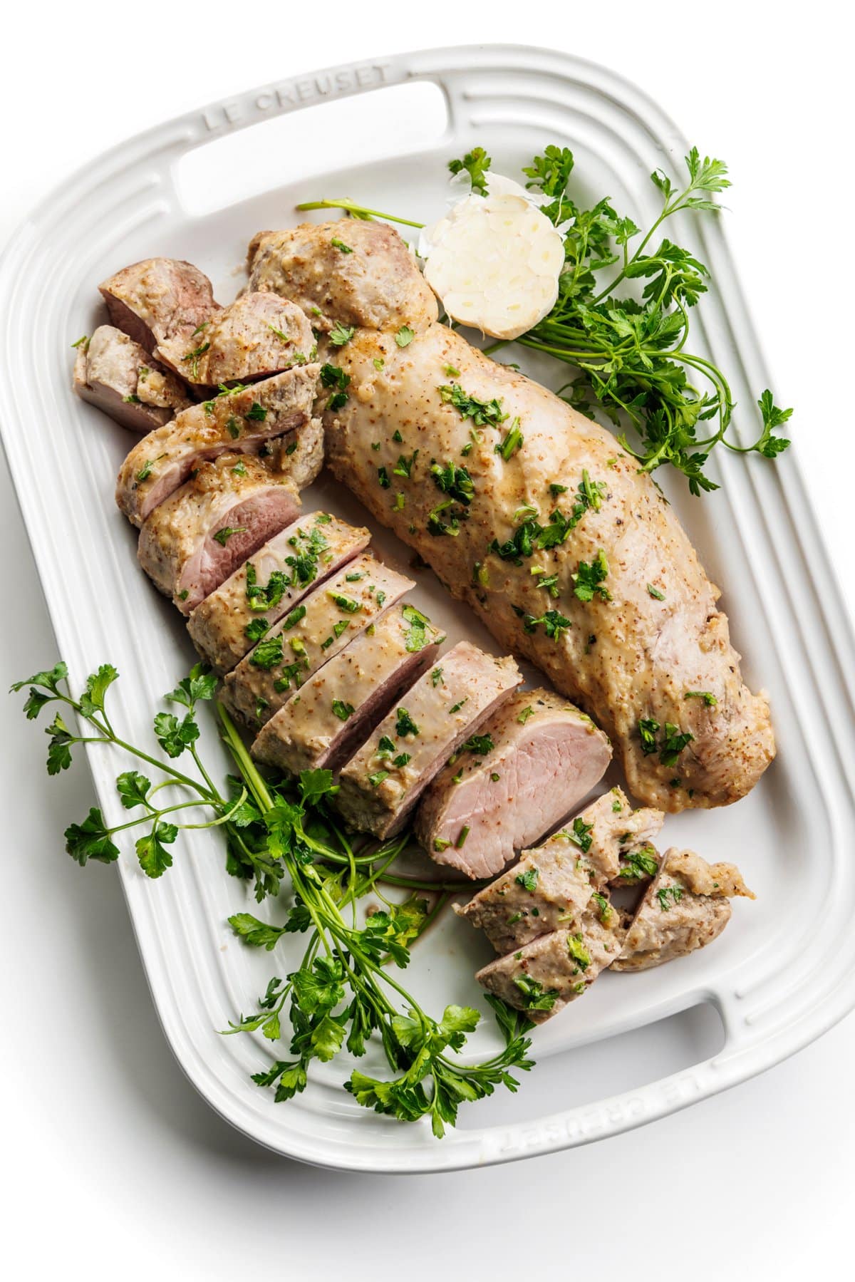 Cooked pork tenderloin laid out on a white platter, garnished with fresh parsley.