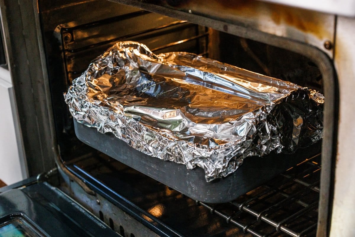 Beef brisket in roasting pan covered in foil in the oven.